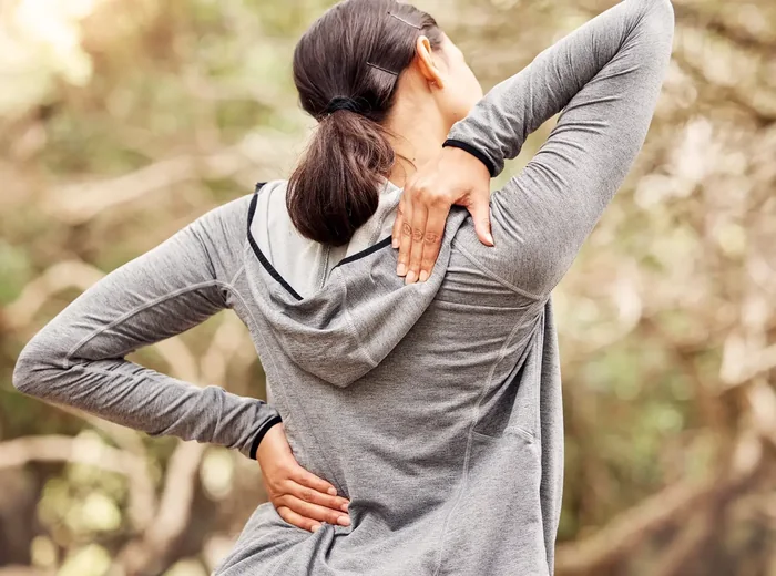 Person holding their lower back and shoulder in discomfort