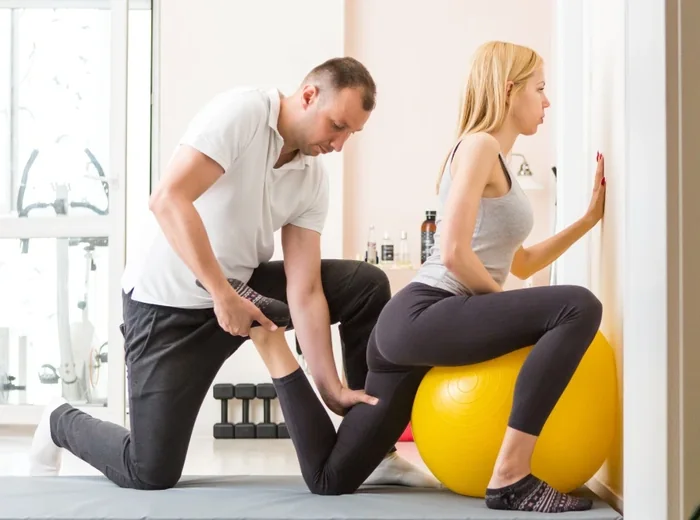 Therapist treating a runner's leg while she balances on an exercise ball