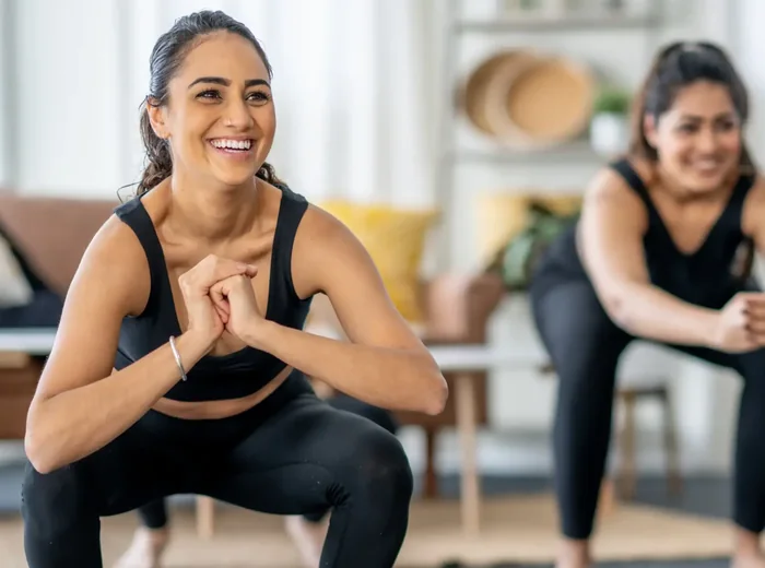 Two women holding a squat during a guided home exercise session